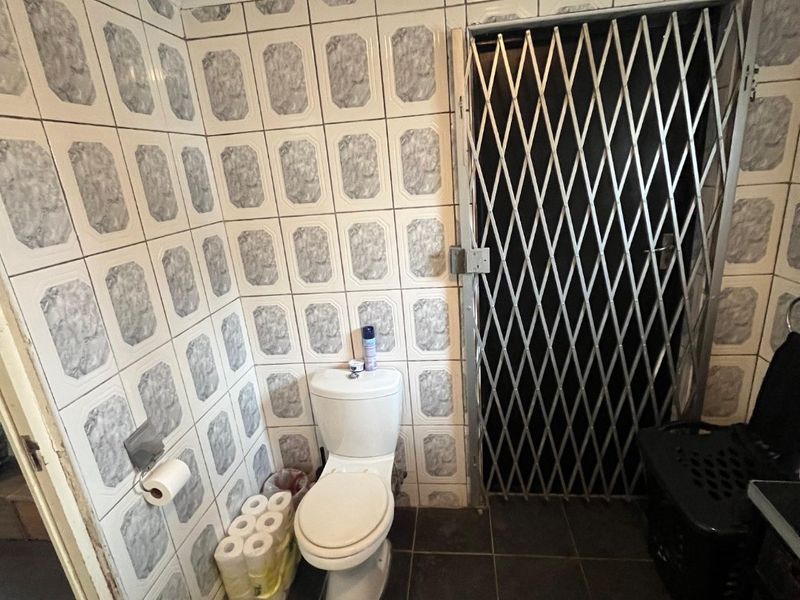 A functional bathroom featuring ceramic wall and floor tiling, equipped with a standard toilet and a security gate installed at the doorway.