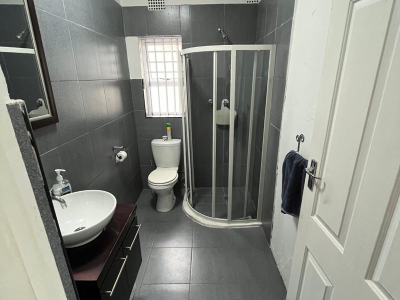 A functional bathroom featuring dark grey wall and floor tiles, a modern vessel sink vanity, a corner shower enclosure, and a toilet.