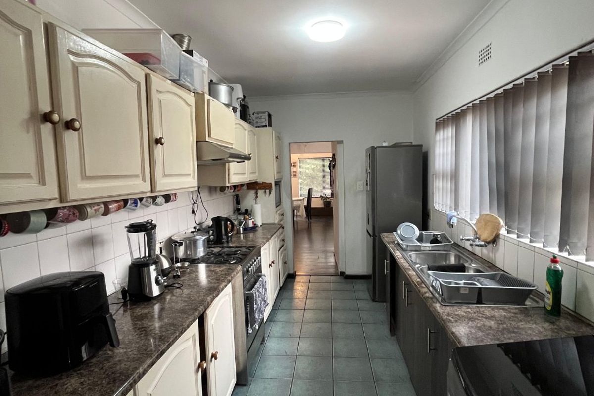 A functional galley-style kitchen featuring laminate countertops, tiled flooring, built-in cabinetry, and a double bowl stainless steel sink.