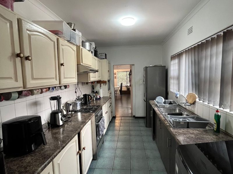 A functional galley-style kitchen featuring laminate countertops, tiled flooring, built-in cabinetry, and a double bowl stainless steel sink.