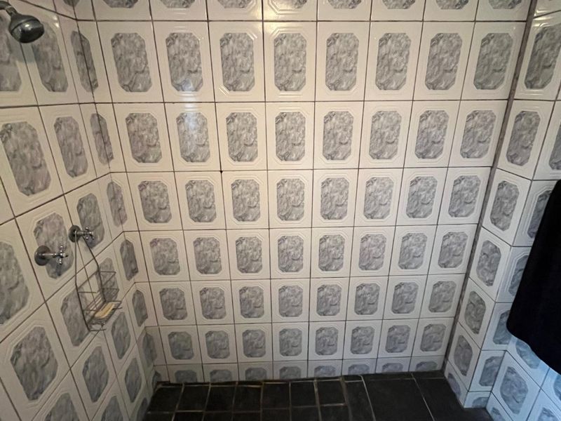 A shower enclosure featuring dated patterned wall tiles and dark floor tiles, equipped with a standard shower head and mixer.