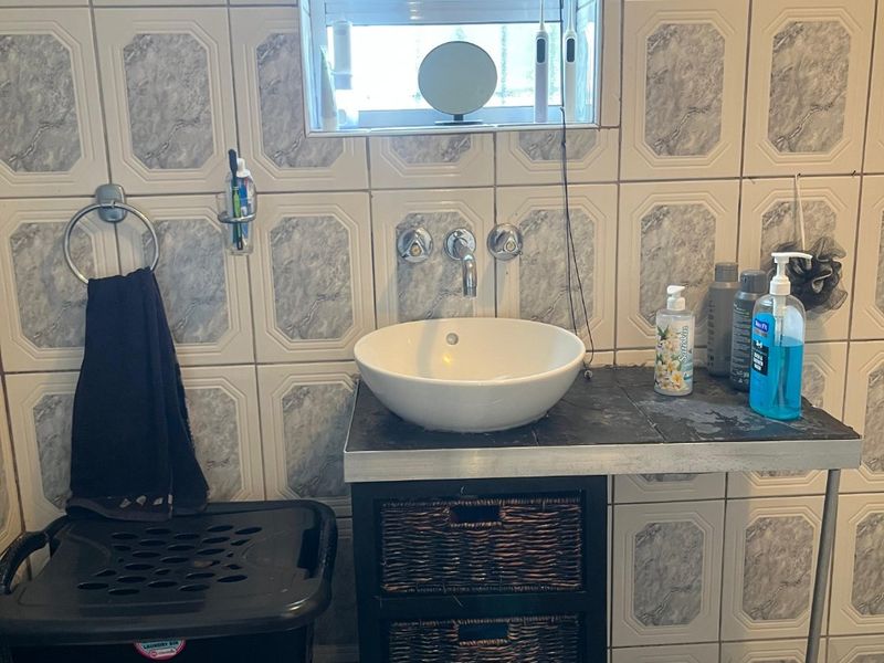 A compact bathroom featuring a vessel sink, wall-mounted faucet, and dated decorative wall tiling.