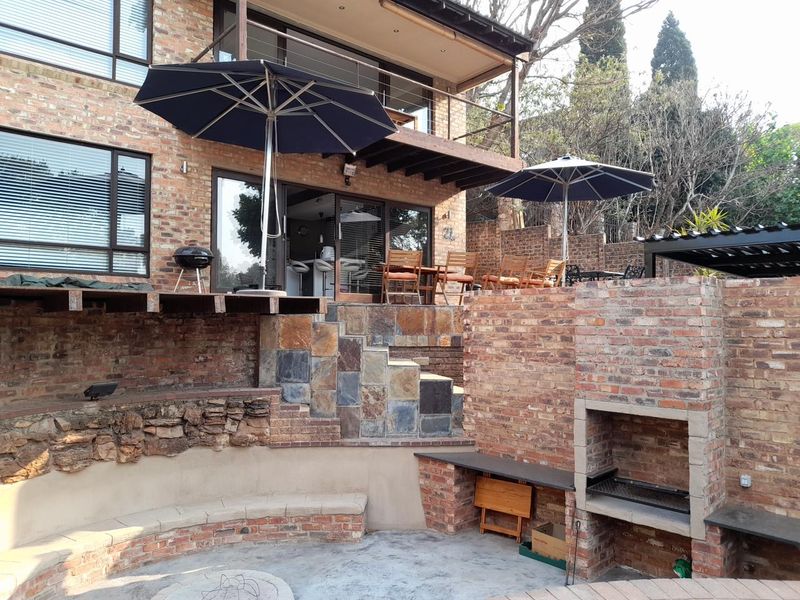 Multi-level rear exterior featuring an exposed brick facade, built-in braai area, stone-clad stairs, and a spacious balcony overlooking the patio.