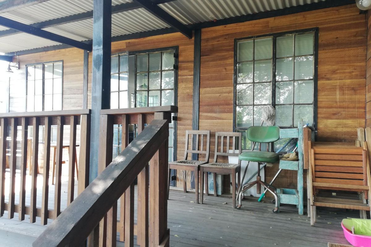 A covered timber patio featuring wood wall cladding, steel-framed windows, and a corrugated metal roof, offering a rustic outdoor living space.