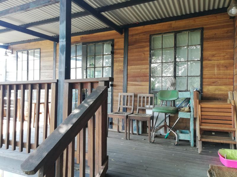 A covered timber patio featuring wood wall cladding, steel-framed windows, and a corrugated metal roof, offering a rustic outdoor living space.