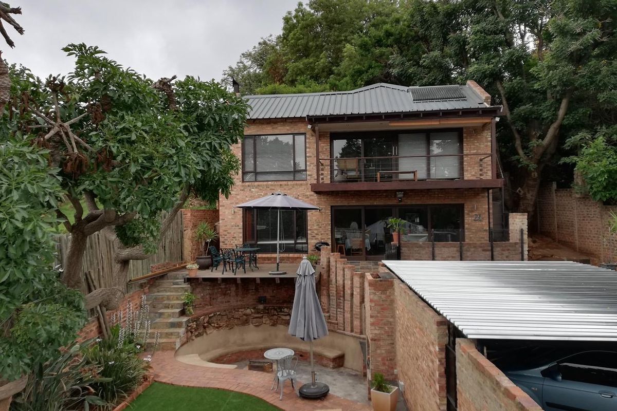 Rear view of a two-story brick house featuring a balcony, timber deck, sunken fire pit area, and a carport, set within a landscaped garden.