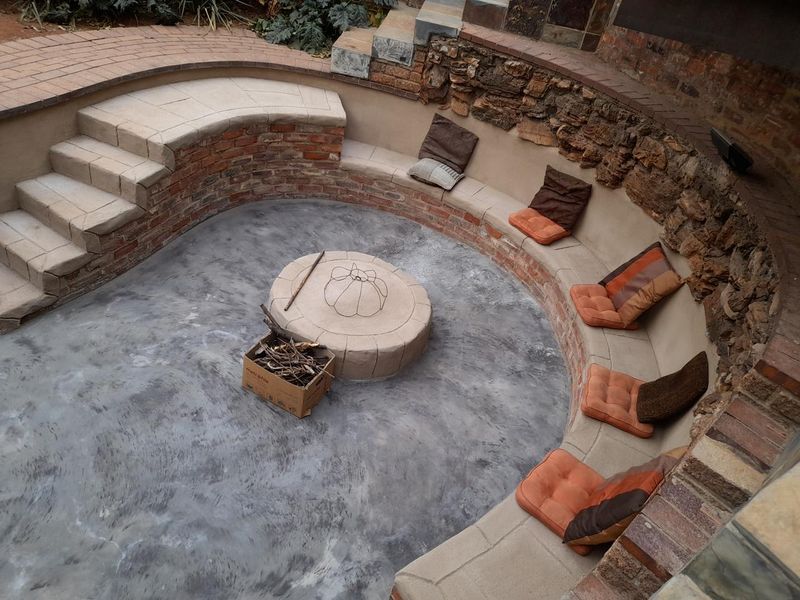 A sunken outdoor fire pit area featuring circular stone seating, stone retaining walls, and concrete flooring, perfect for outdoor entertaining.