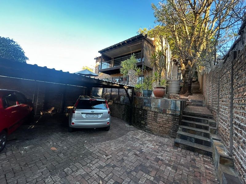 Front exterior view featuring a covered carport, brick paved driveway, stone retaining walls, and a staircase leading to the upper level balcony.