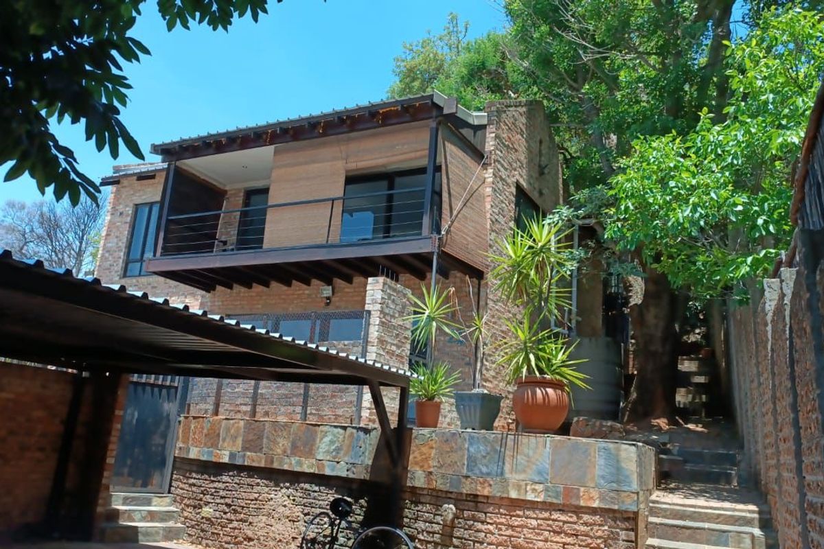 Rear view of a multi-level house featuring exposed brickwork, a timber balcony with metal railings, and stone retaining walls set against a natural backdrop.