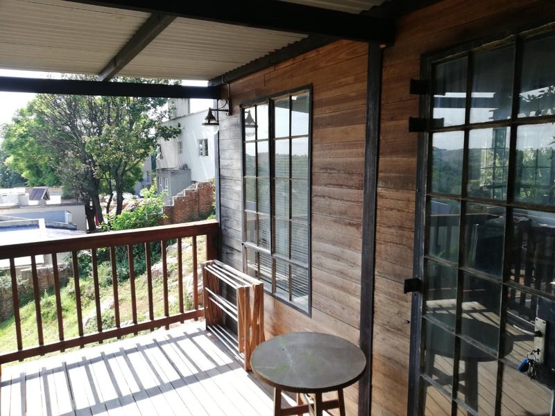 A covered timber balcony featuring steel-framed windows and a wooden balustrade, offering an elevated outdoor space with a rustic aesthetic.