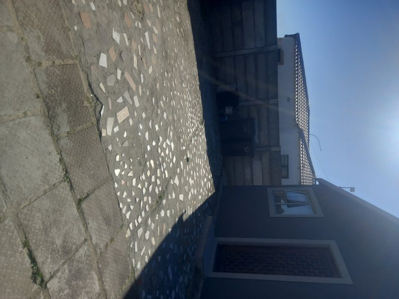 A rear exterior view showing a paved courtyard area enclosed by a precast concrete boundary wall and the side elevation of the house.