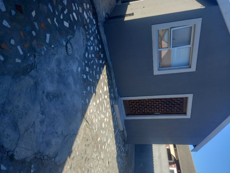 Rear exterior view of the property featuring a paved patio area, a single door, and a window.