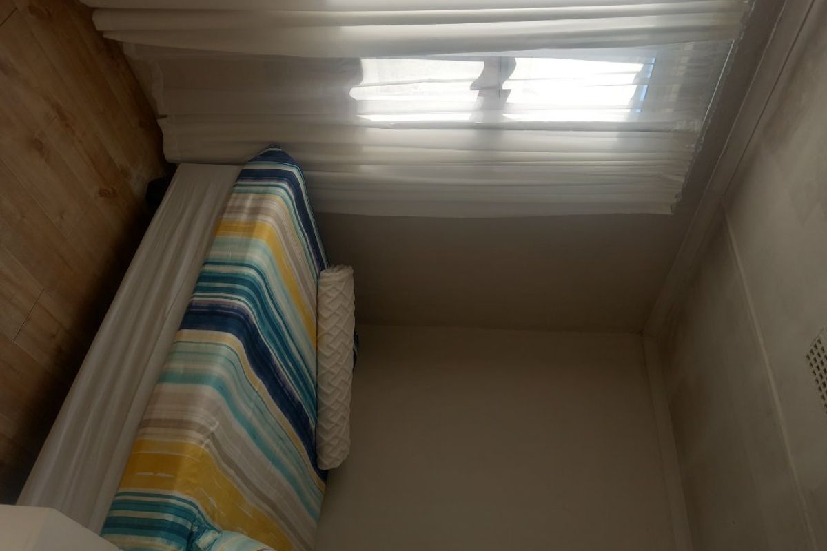 A bedroom featuring laminate flooring and a ceiling vent, showing signs of wall and ceiling discoloration requiring maintenance.