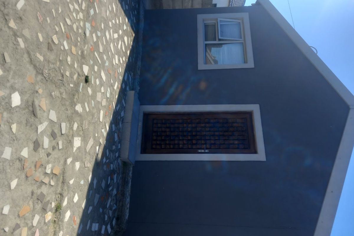 A side view of the property featuring a grey exterior wall, a timber door, a uPVC window, and a paved outdoor area.