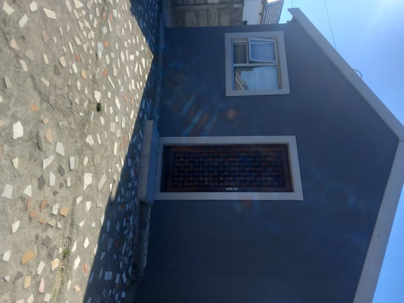 A side view of the property featuring a grey exterior wall, a timber door, a uPVC window, and a paved outdoor area.