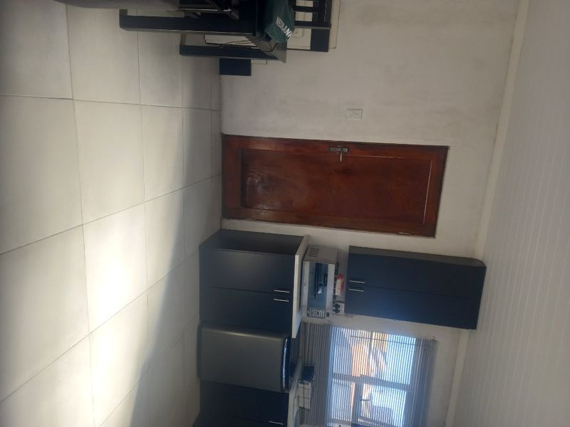 A compact kitchen area featuring dark built-in cabinetry, tiled flooring, and a timber door, requiring cosmetic updates to improve the overall aesthetic.