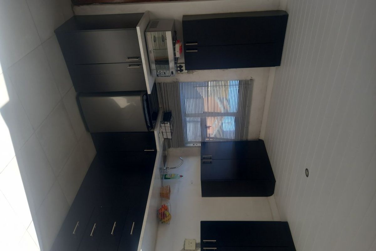 A compact kitchen featuring dark cabinetry, a stainless steel sink, and tiled splashbacks, offering a functional workspace with potential for cosmetic updates.