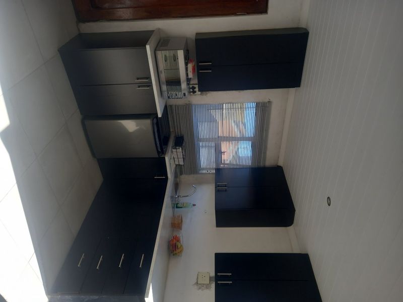 A compact kitchen featuring dark cabinetry, a stainless steel sink, and tiled splashbacks, offering a functional workspace with potential for cosmetic updates.