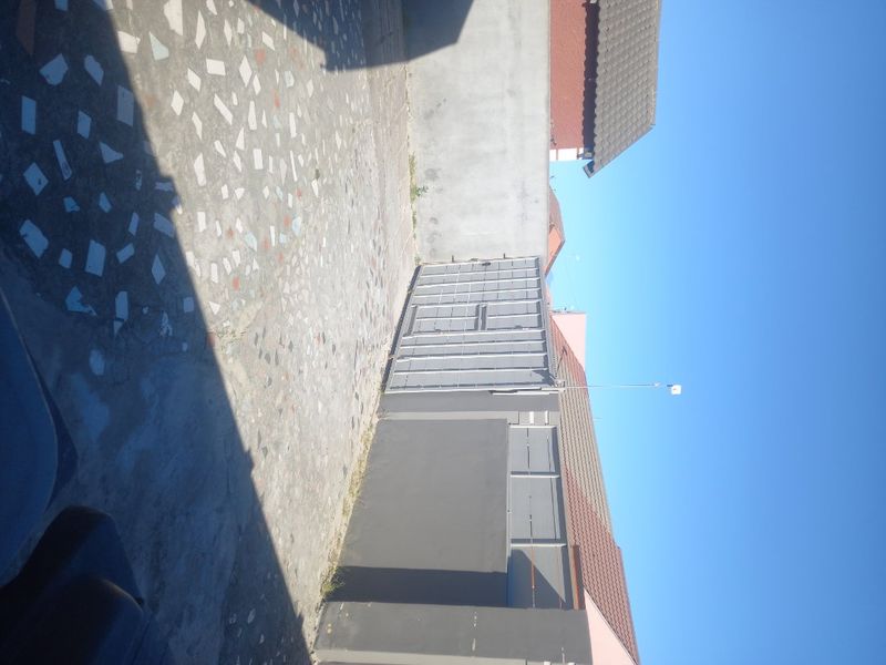 A rear exterior view showing a paved courtyard area, boundary wall, and metal gate access.