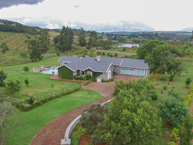 Aerial view of a spacious residential property featuring a large landscaped garden, swimming pool, paved driveway, and a double garage.