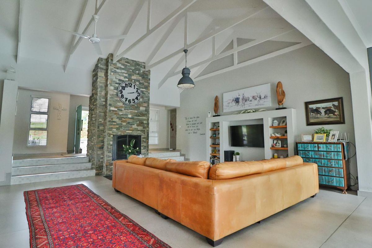Spacious living room featuring a vaulted ceiling with exposed trusses, a prominent stone-clad fireplace, and a built-in media unit with tiled flooring.