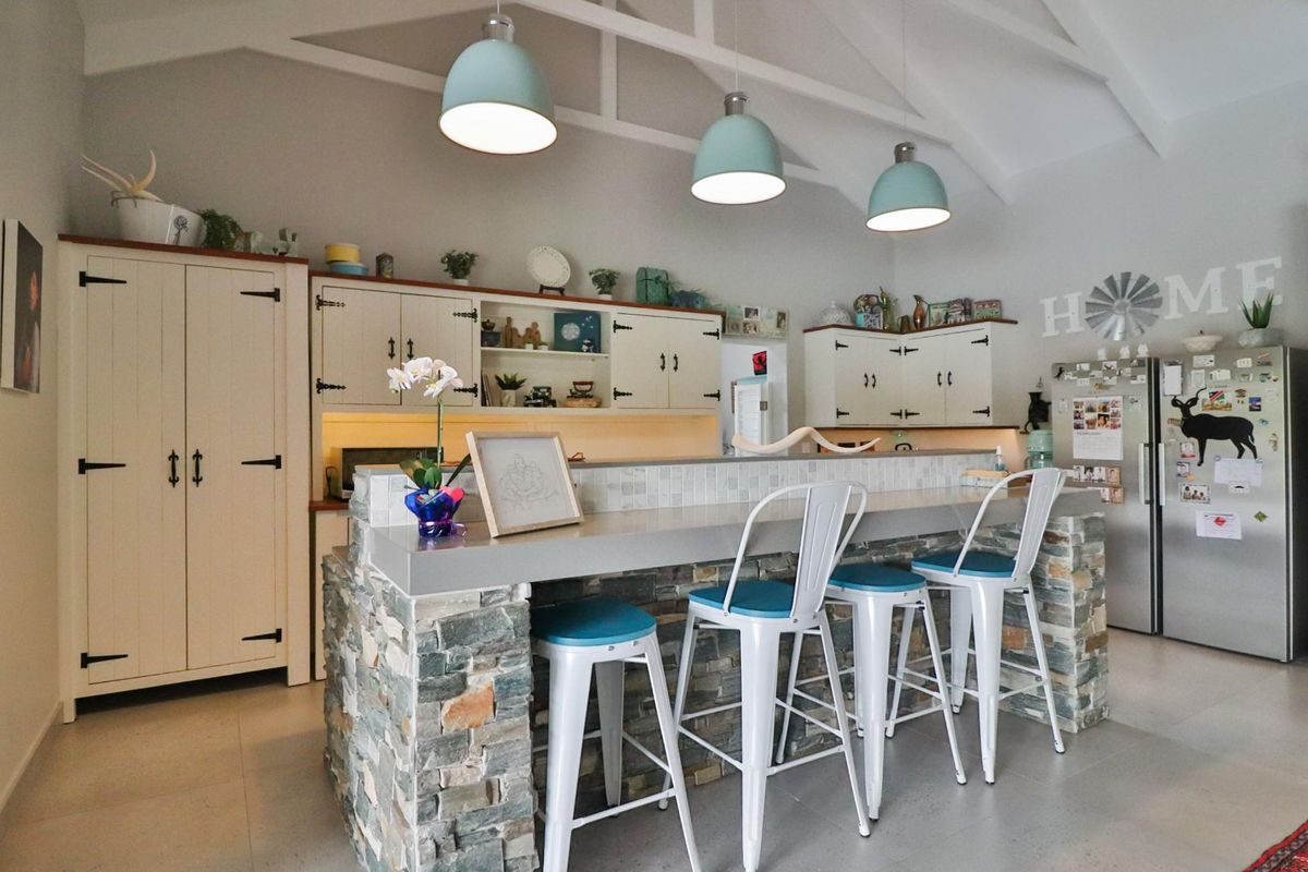 A well-lit kitchen featuring a stone-clad breakfast bar, vaulted ceilings, and ample built-in cabinetry with a modern, rustic aesthetic.