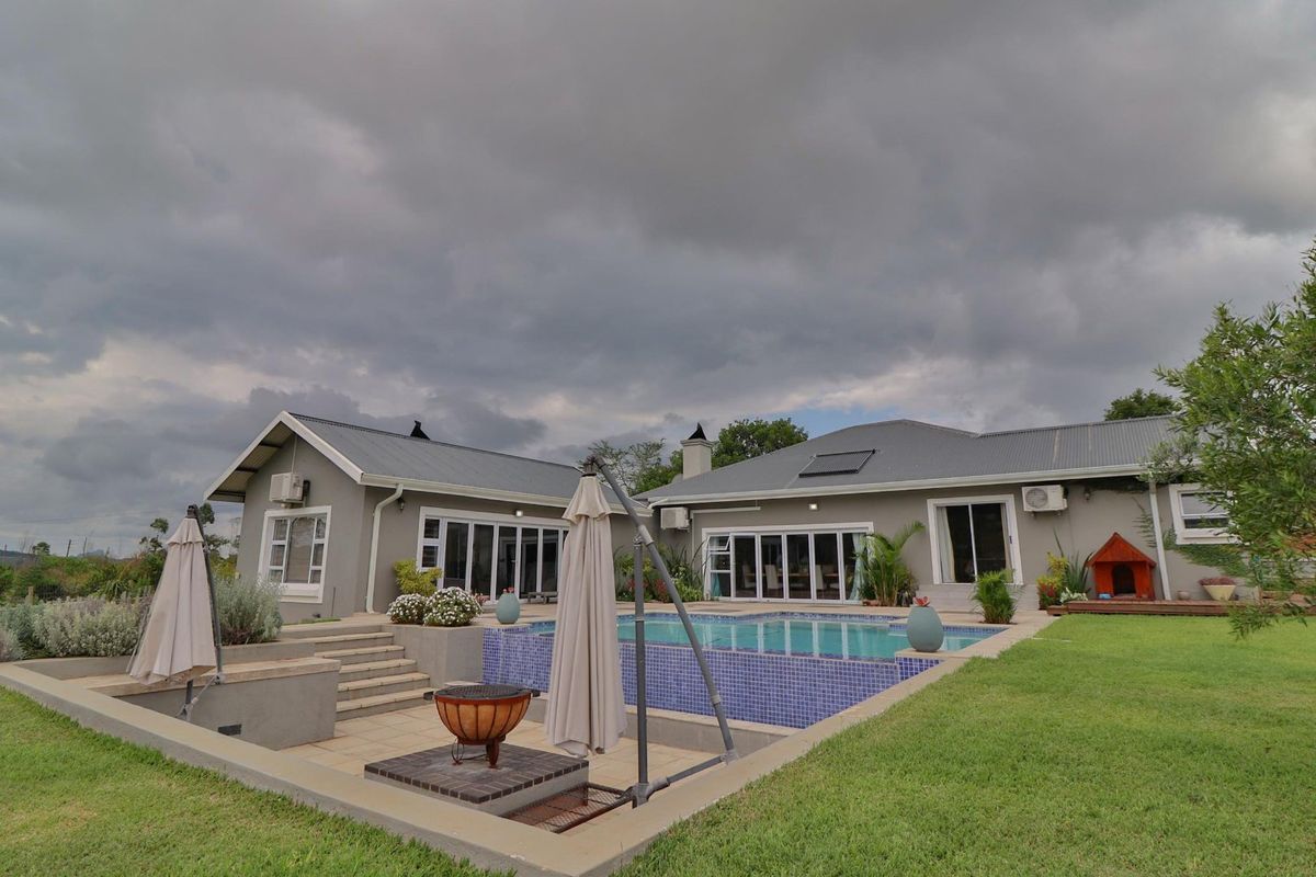 Rear exterior view featuring a swimming pool with tiled surround, raised deck area, landscaped lawn, and access to the home via sliding glass doors.