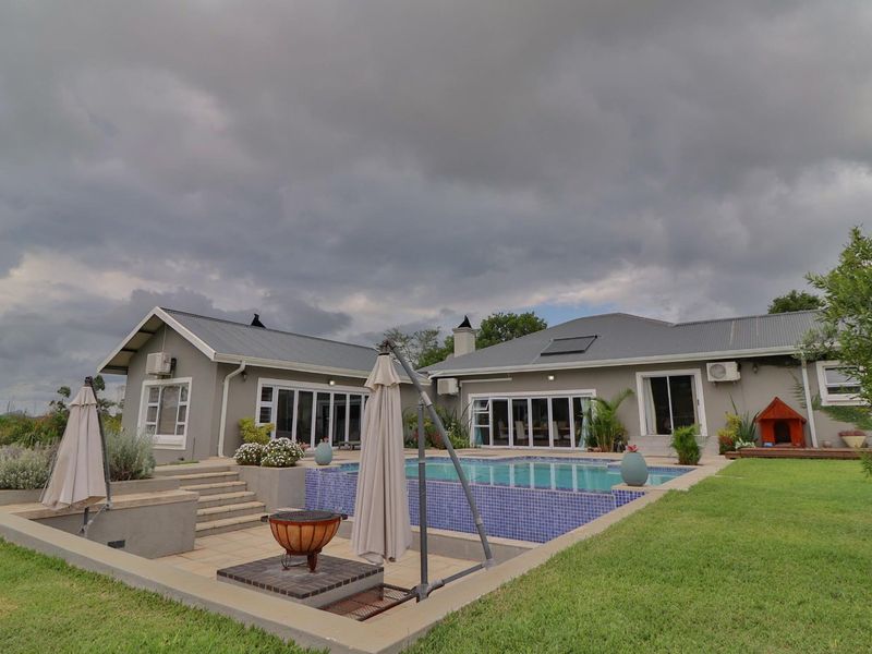 Rear exterior view featuring a swimming pool with tiled surround, raised deck area, landscaped lawn, and access to the home via sliding glass doors.