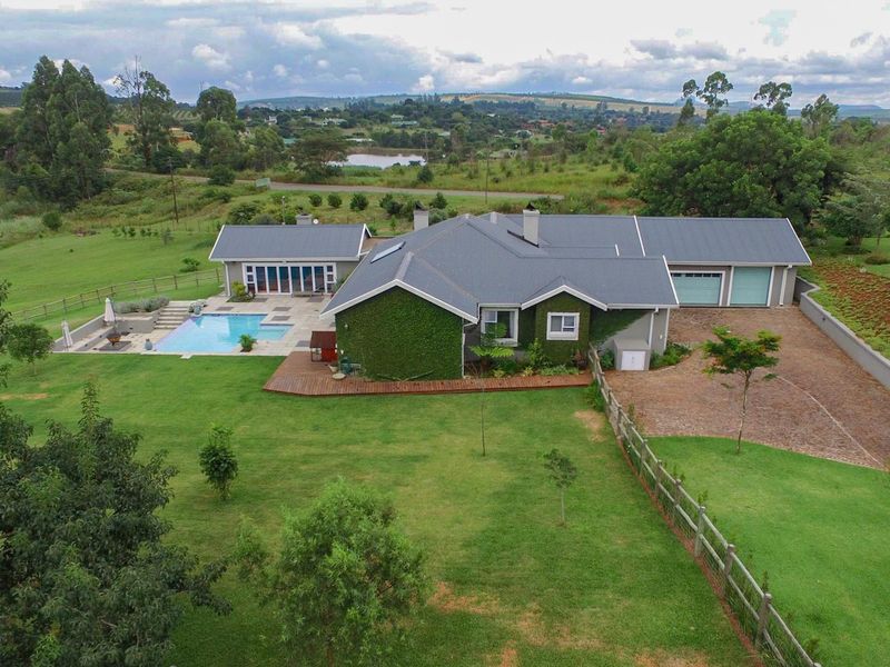 Aerial view of a well-maintained residential property featuring a swimming pool, timber decking, metal roofing, and a spacious landscaped garden.
