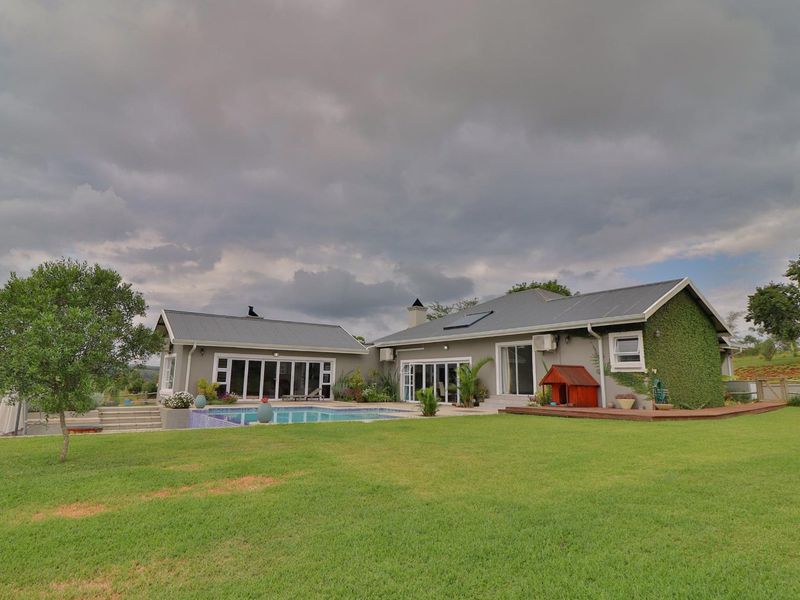 Rear view of the property featuring a swimming pool, timber decking, and expansive lawn area under a cloudy sky.
