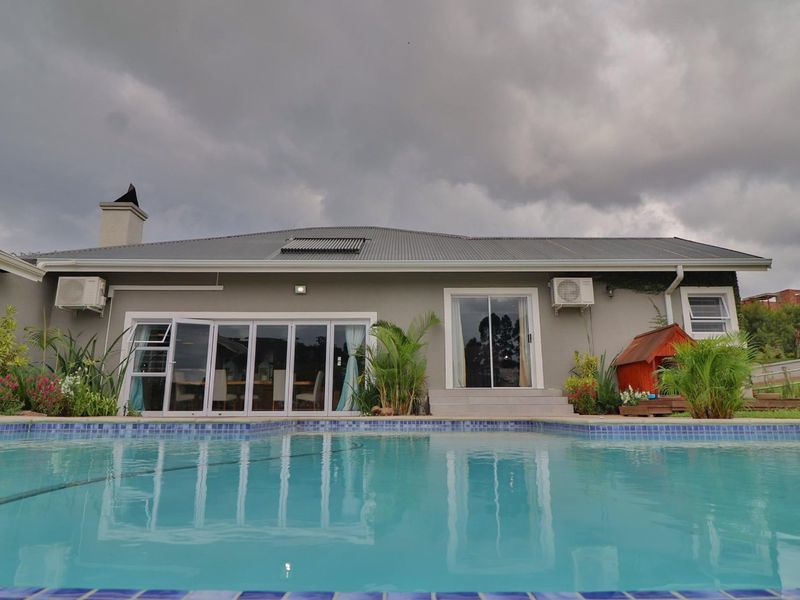 Rear exterior view of the property featuring a swimming pool, tiled surround, and direct access to the living areas through folding and sliding glass doors.