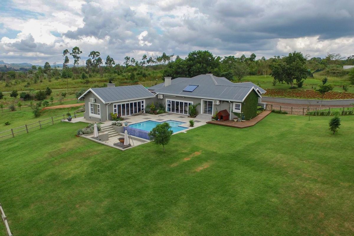 Aerial view of a modern residence featuring a swimming pool, expansive lawn, timber decking, and a metal roof with integrated solar heating.