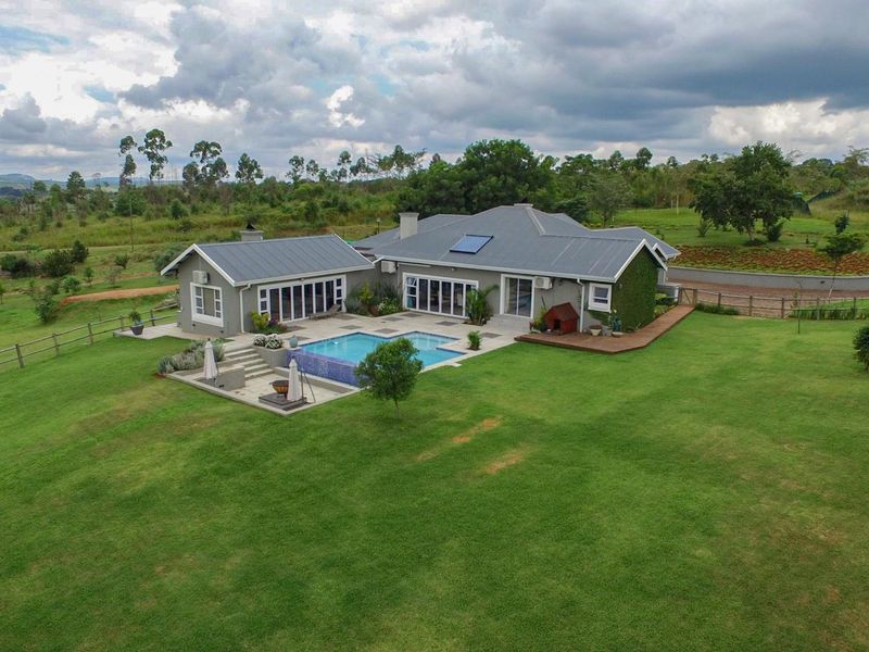 Aerial view of a modern residence featuring a swimming pool, expansive lawn, timber decking, and a metal roof with integrated solar heating.