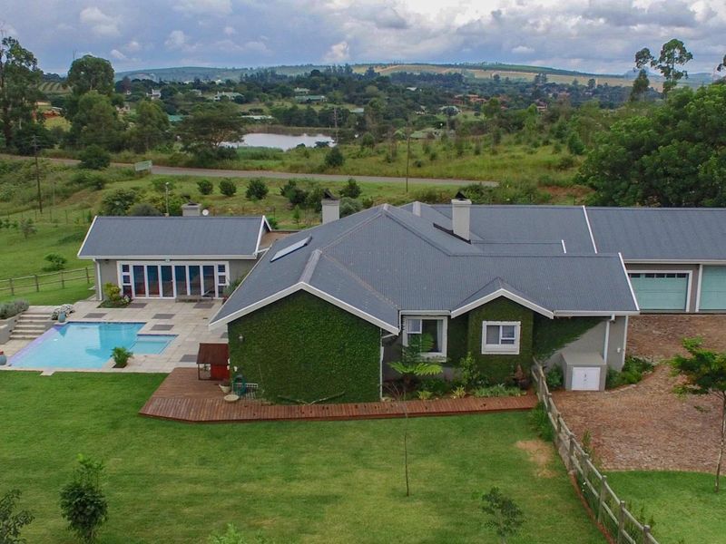 Aerial view of a residential property featuring a swimming pool, timber decking, paved patio, metal roof, and a spacious garden with scenic landscape views.