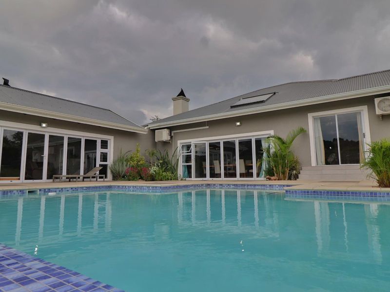 A well-maintained swimming pool area featuring a tiled pool, multiple sliding glass doors providing indoor-outdoor flow, and a modern exterior facade.