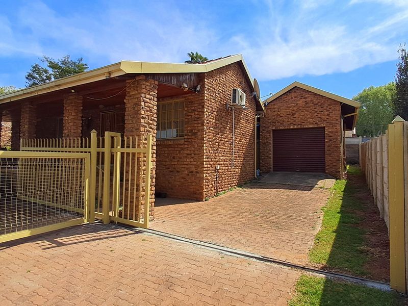 Front view of a face brick house featuring a paved driveway, secure metal gate, attached garage, and a covered patio area.