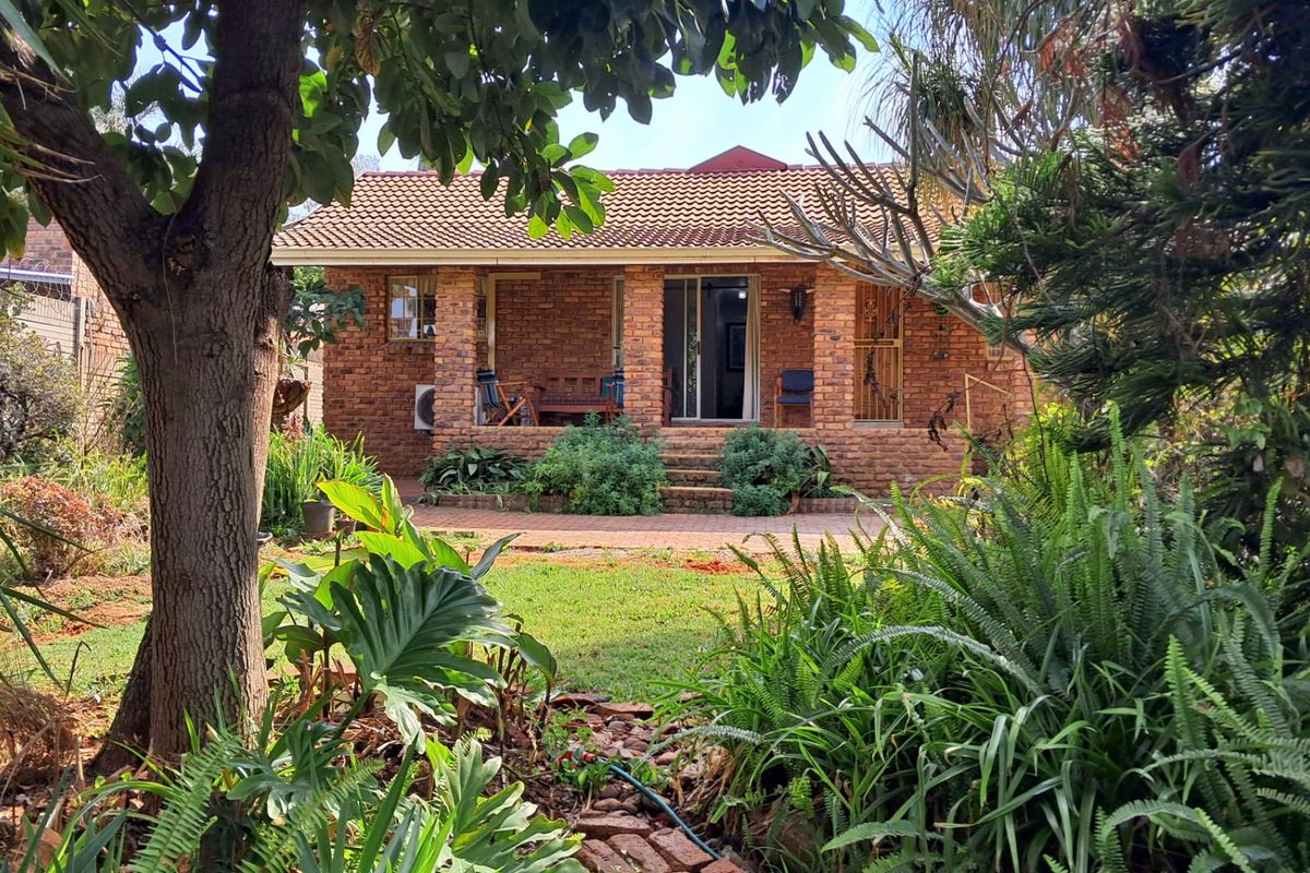 A rear view of a brick house featuring a covered patio, sliding glass doors, and a mature garden setting.