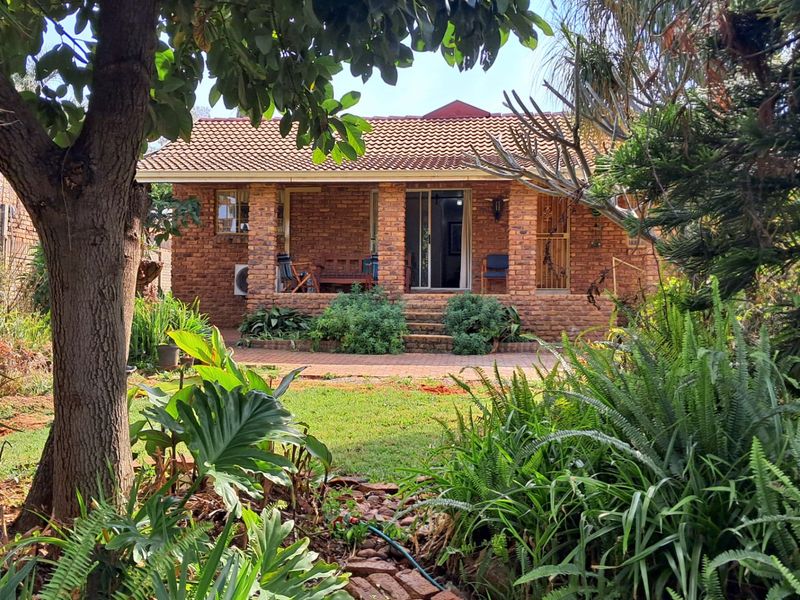 A rear view of a brick house featuring a covered patio, sliding glass doors, and a mature garden setting.