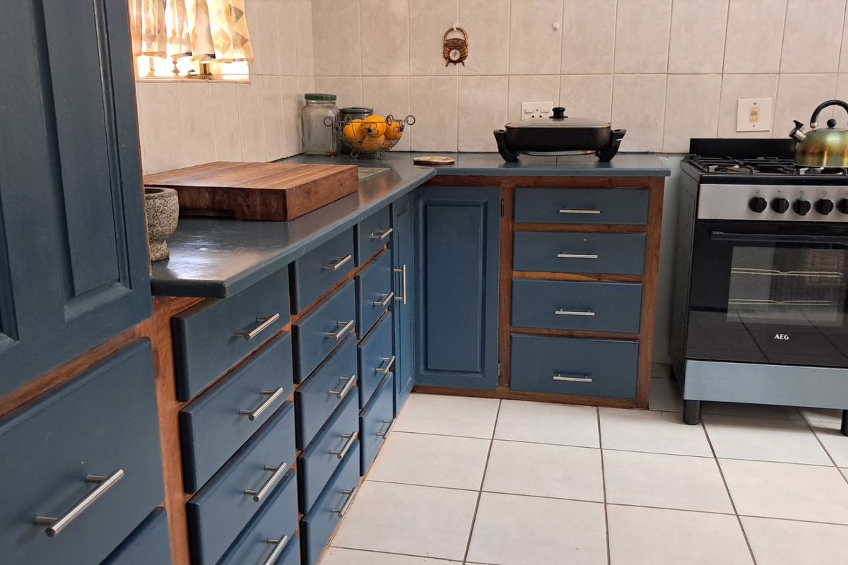 A functional kitchen featuring blue painted cabinetry, tiled backsplash, and a freestanding oven, offering a practical layout with ample storage space.
