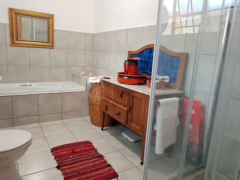 A functional bathroom featuring a pedestal basin, a built-in bathtub, and a separate glass-enclosed shower with neutral wall and floor tiling.