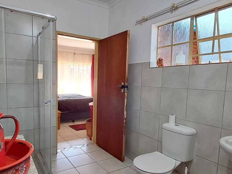 A functional bathroom featuring a glass-enclosed shower, pedestal basin, and toilet, with neutral wall and floor tiling throughout.
