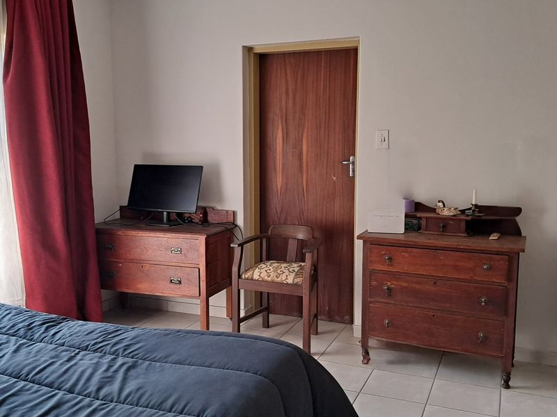 A functional bedroom featuring tiled flooring, built-in cupboards, and a timber door, offering a neutral base for potential interior updates.