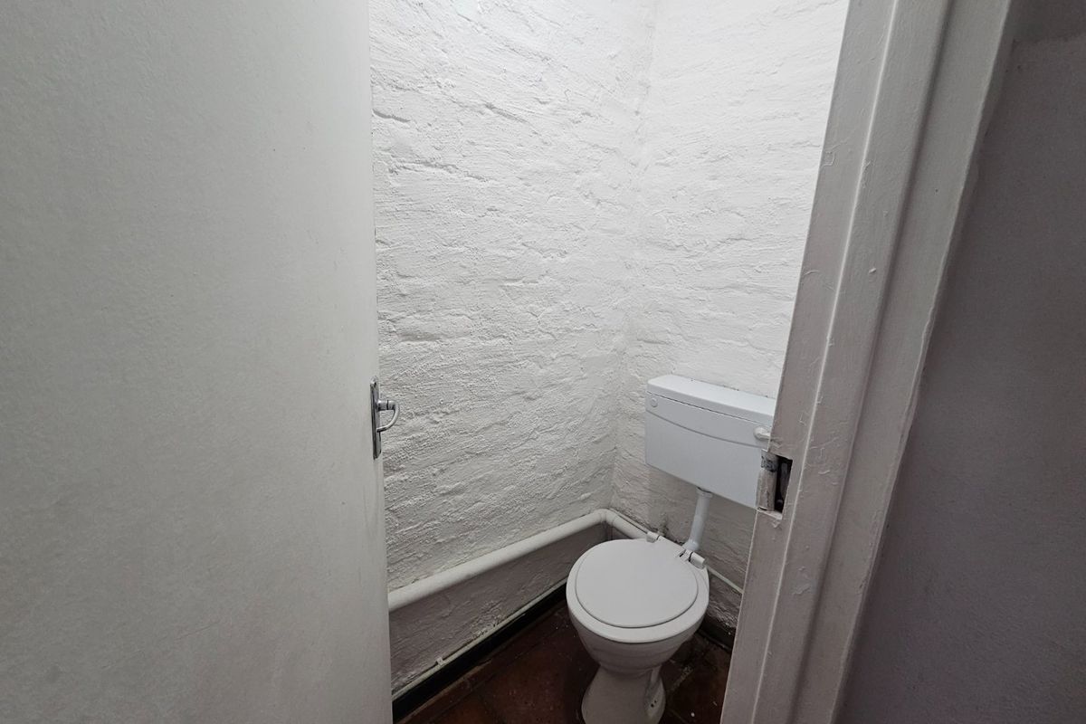 A compact, functional bathroom featuring a standard toilet, exposed brick walls, and tiled flooring, requiring cosmetic updates to improve its overall aesthetic.