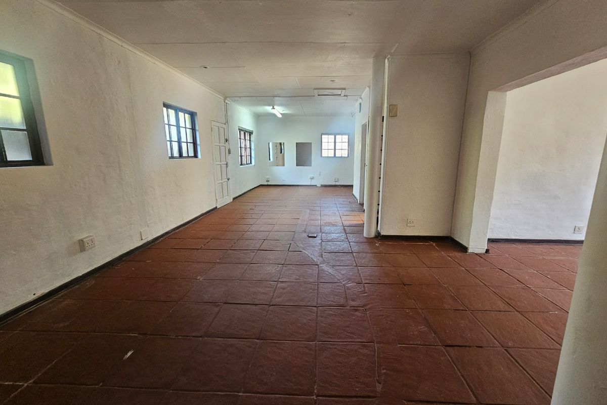 An empty, open-plan living area featuring terracotta tiled flooring, multiple windows, and a neutral wall finish, offering a blank canvas for renovation.