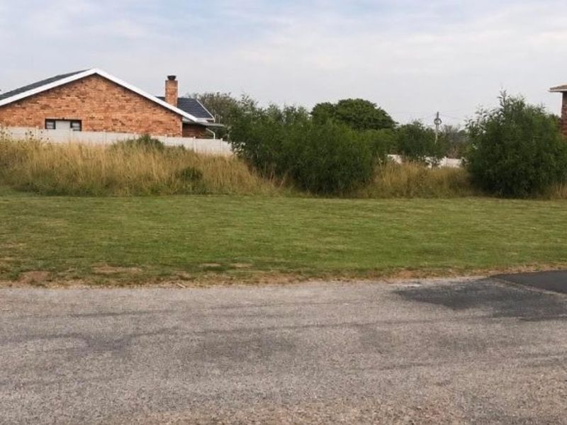 A vacant residential plot featuring a grass lawn and boundary fencing, situated in a developed neighborhood.
