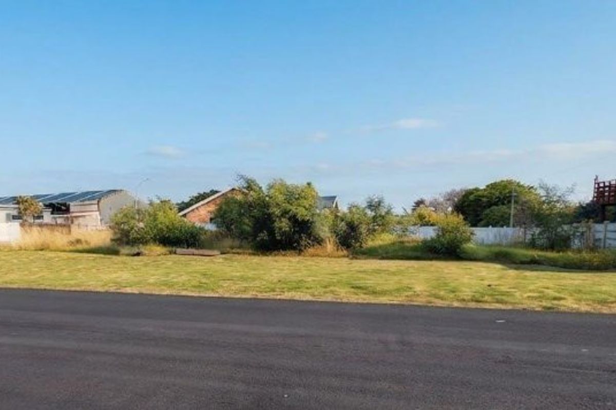 A vacant residential plot featuring a level grassed surface, bordered by precast concrete walls and accessible via a paved road.