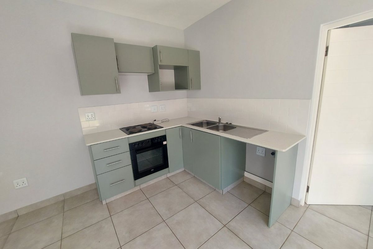 A clean, modern kitchen featuring sage green cabinetry, a built-in oven and hob, tiled splashback, and a double sink with dedicated appliance space.