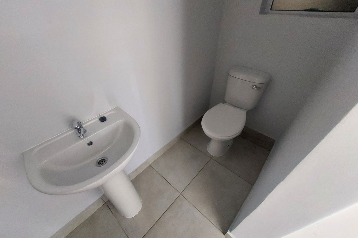 A compact bathroom featuring a white pedestal washbasin and a standard toilet with neutral floor tiling.