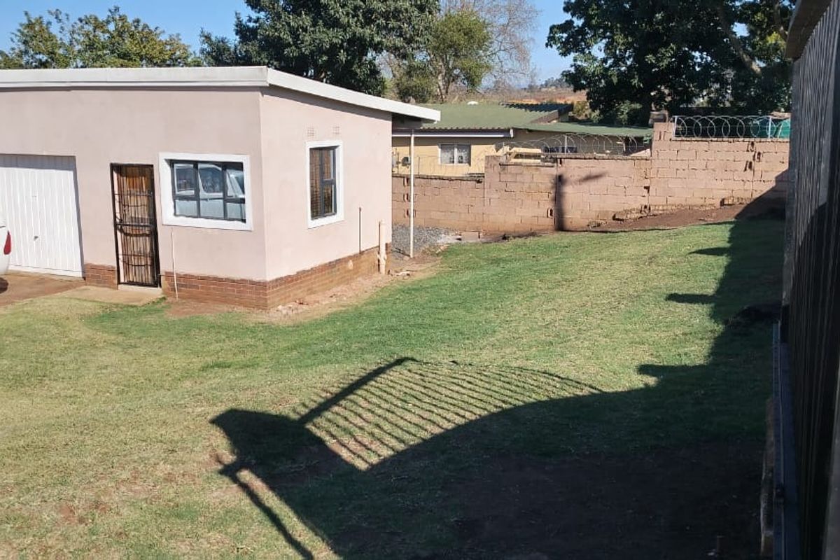 Rear exterior view showing a detached garage, lawn area, and perimeter brick boundary wall with security fencing.
