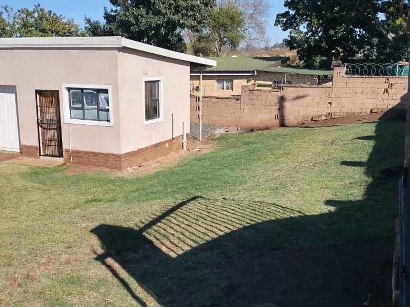 Rear exterior view showing a detached garage, lawn area, and perimeter brick boundary wall with security fencing.